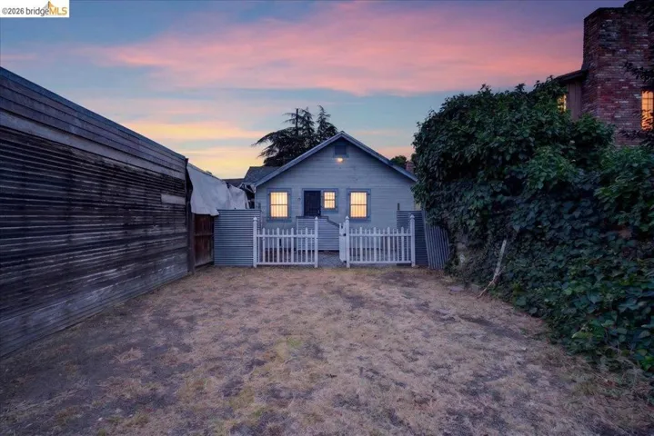 Rear exterior featuring a picket fence entrance, wood siding, and mature perimeter foliage
