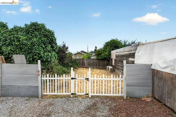 Gravel entry area opening to a fenced rear yard with a white picket gate