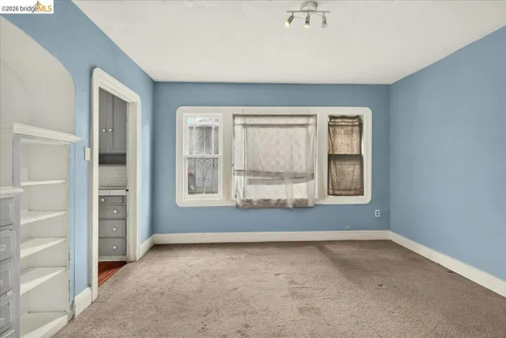 Carpeted room featuring a built-in bookshelf, track lighting, and a window with security bars