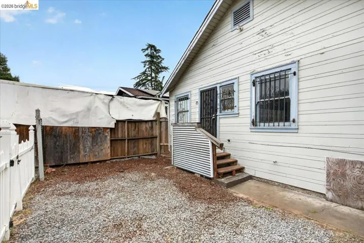 Exterior featuring horizontal siding, multiple windows with security bars, and a wooden staircase leading to an entry door