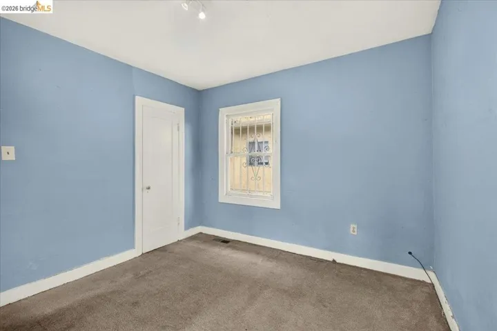 Room featuring light blue walls, white trim, and a window with decorative security bars