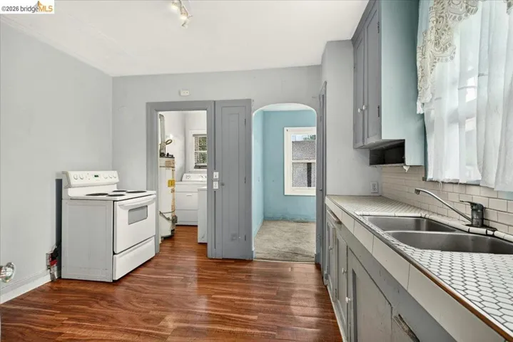 Kitchen featuring wood-finish flooring, a white electric range, and gray cabinetry with a dual-basin stainless steel sink
