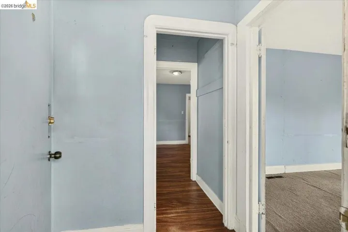 Interior hallway featuring light blue walls, white trim, and wood-finish flooring