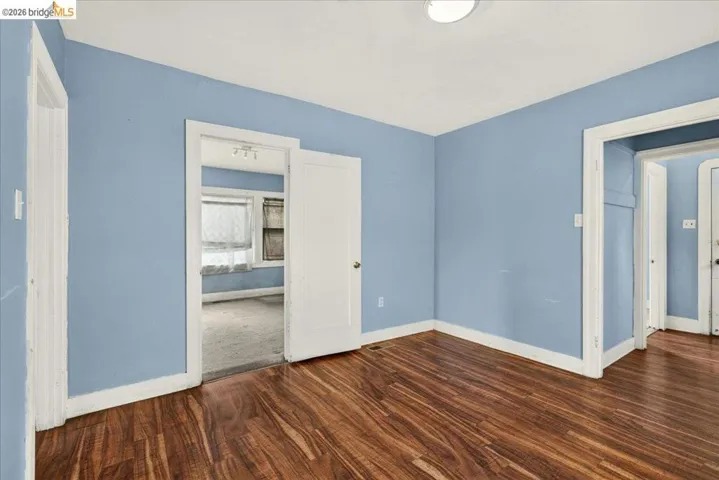 Room featuring wood-finish flooring, light blue wall paint, white baseboards, and white ceiling