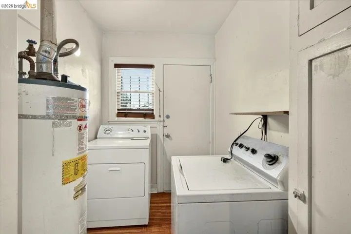 Dedicated utility space featuring wood-finish flooring, a window with blinds, and white walls