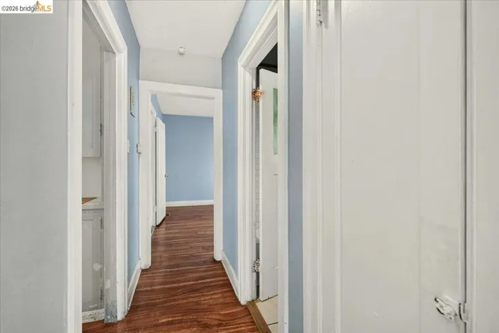 Interior hallway featuring wood-finish flooring, light blue wall paint, white trim, and multiple doorways