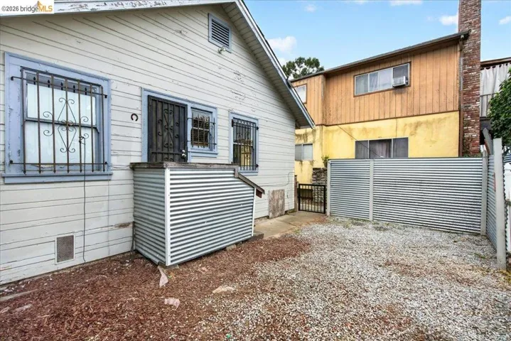 Exterior siding with a window featuring decorative security bars, a corrugated metal fence, and a gravel ground cover