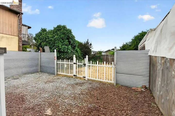 Gravel yard area featuring corrugated metal fencing and a white picket gate