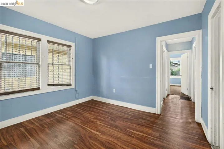 Room featuring wood-finish flooring, two windows with blinds and security bars, and a light blue wall finish