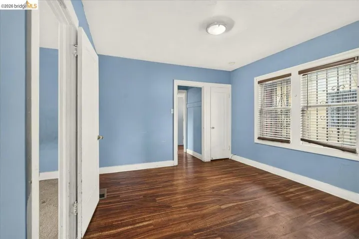 Room featuring wood-finish flooring, two window openings with blinds, a ceiling-mounted light fixture, and a built-in closet with a white door