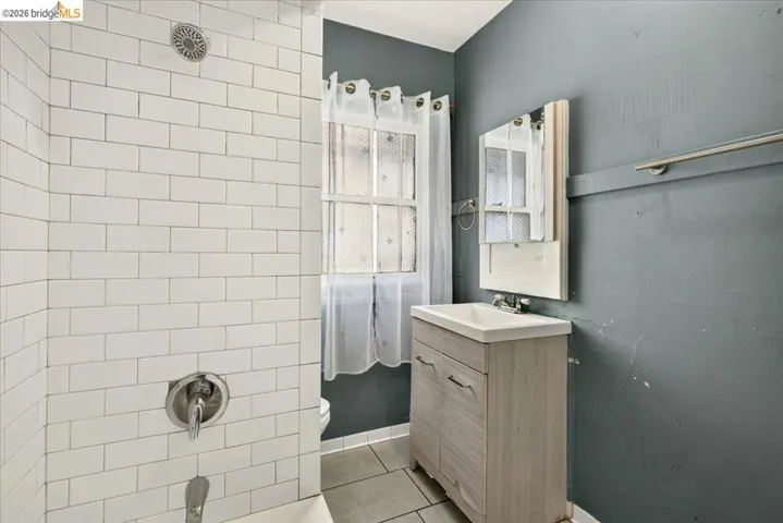 Bathroom featuring a tub/shower combination with white subway tile surround, a single vanity with a light wood-finish cabinet, a wall-mounted mirror, and tile flooring