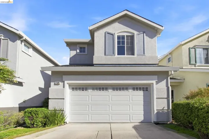 Two-story stucco residence featuring a ground-level garage, second-story window with louvered shutters, and a sloped roofline