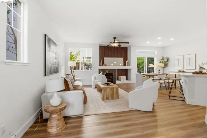 Open-concept living area featuring wood-finish flooring throughout, a modern fireplace with a wood-paneled accent wall, a ceiling fan, and recessed lighting
