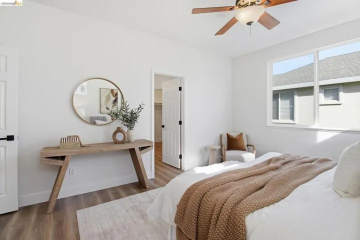Bedroom featuring a large window, wood-finish flooring, a ceiling fan with light, and a white interior door with black hardware