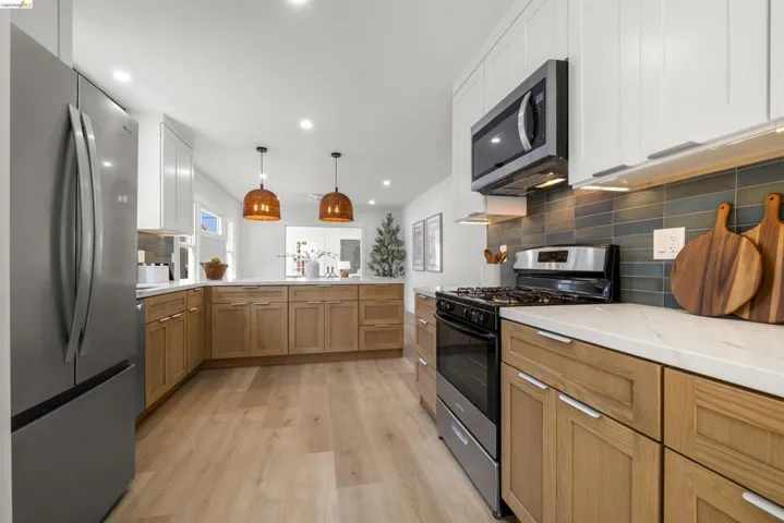 Modern kitchen featuring stainless steel appliances, two-tone cabinetry with light wood-finish bases and white uppers, white countertops, a dark blue-gray tile backsplash, and light wood-finish flooring