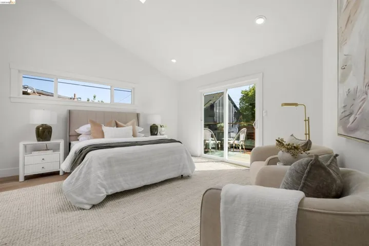 Vaulted ceiling bedroom featuring white walls, recessed lighting, horizontal transom windows, light wood-finish flooring, and a sliding glass door opening to an outdoor patio