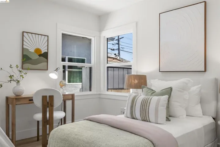 Bright room featuring two large windows with white trim, light wood-finish flooring, a white headboard, and white walls