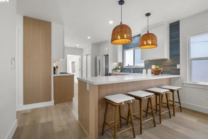 Open-concept kitchen featuring a large island with white countertop, integrated cabinetry, wood-finish flooring, and a blue tile backsplash