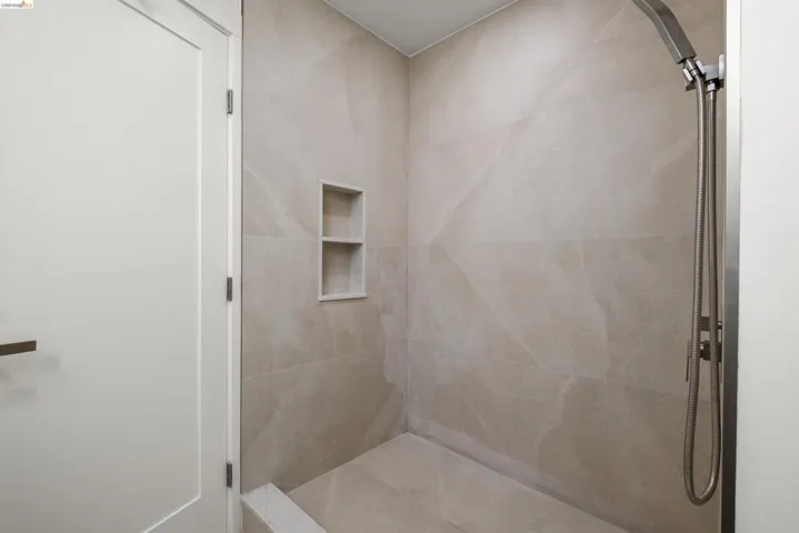 Walk-in shower featuring large format wall and floor tiling, a built-in shower niche with two shelves, and a contemporary shower head fixture