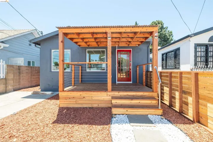 Exterior featuring a wood deck with cable railing, a red entry door, and a wood pergola with a corrugated roof