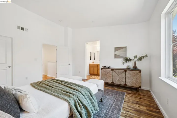 Bedroom featuring wood-finish flooring, white walls, and a large window with exterior foliage visible