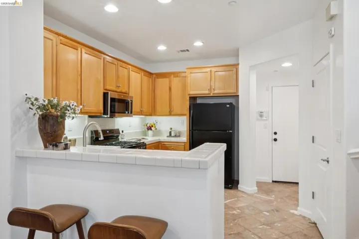 Kitchen featuring a breakfast bar with tile countertop, wood cabinetry, built-in microwave, stainless steel sink with gooseneck faucet, and recessed lighting