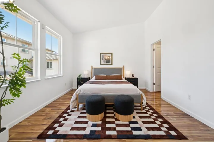 Bright bedroom featuring two large windows, wood-finish flooring, a vaulted ceiling, and white baseboards