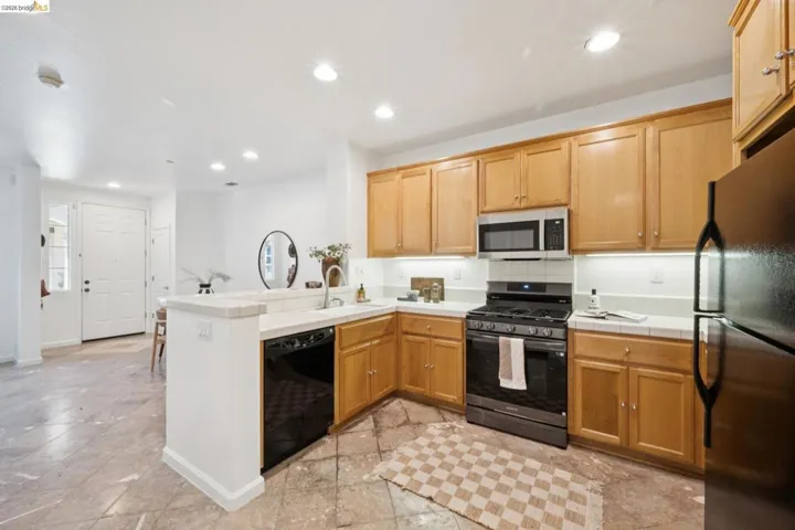 Kitchen featuring wood cabinetry, stainless steel microwave, gas range, black dishwasher, and a stainless steel refrigerator