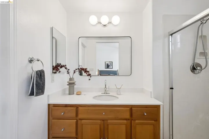 Bathroom featuring a wood-finish vanity with a light-toned countertop, an undermount sink, and a framed mirror