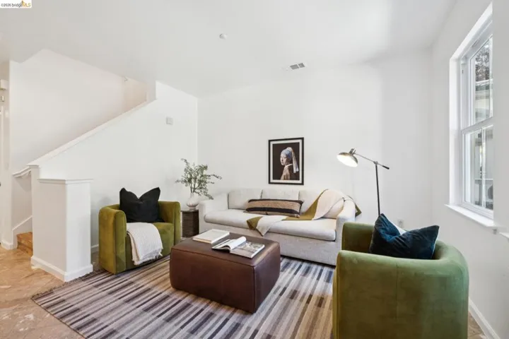 Bright living area featuring white walls, a large window, a staircase with white balustrade, and light-toned flooring
