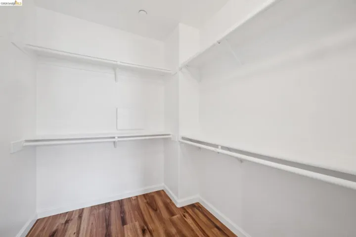 Walk-in closet featuring wood-finish flooring, white walls, and built-in white wire shelving with hanging rods