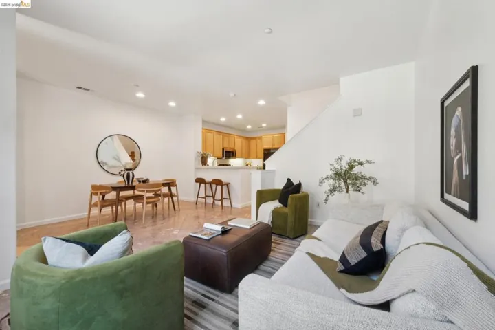 Open-concept living space featuring wood-finish flooring, recessed lighting, a staircase with white risers, and a kitchen with light wood cabinetry and a breakfast bar