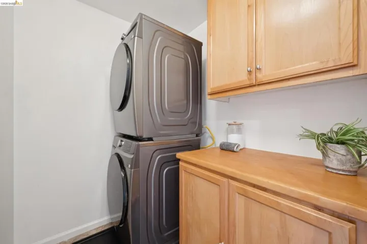 Laundry area featuring stacked appliances, overhead wood-finish cabinetry, and a wood-finish countertop with under-counter storage
