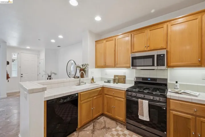 Kitchen featuring light wood cabinetry, white tile countertops, a stainless steel microwave, and a black range