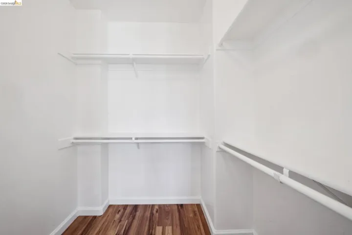 Walk-in closet featuring wood-finish flooring, white walls, white shelving, and white hanging rods