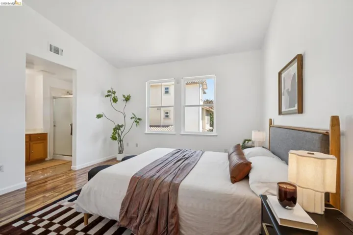 Light-filled bedroom featuring white walls, wood-finish flooring, and two double-hung windows