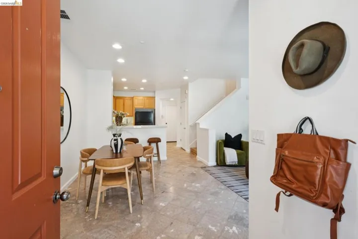 Open-concept living space featuring a bright orange entry door, kitchen with light wood-finish cabinetry, eat-at counter, and recessed lighting, and a staircase with white risers