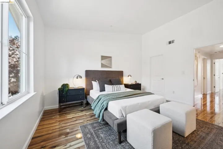 Bedroom featuring wide-plank wood-finish flooring, a large white-framed window, bright white walls, and a recessed doorway