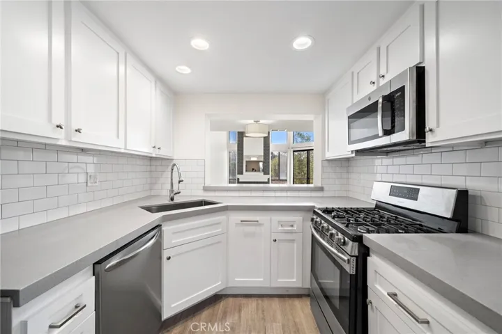Stylish culinary hub boasts modern white shaker cabinetry, elegant grey quartz countertops, a crisp white subway tile backsplash, and premium stainless steel appliances.
