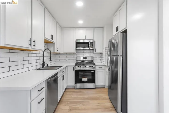 Kitchen with appliances with stainless steel finishes, white cabinetry, light wood-style floors, and light stone counters