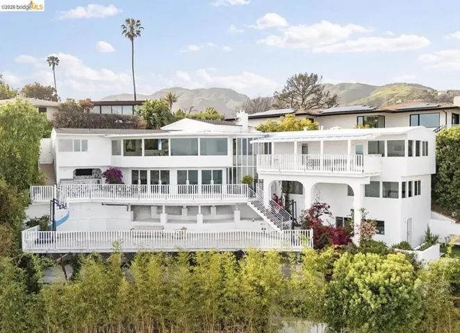 Multi-level white stucco residence featuring extensive balconies with white balustrades, multiple large windows, and a prominent glass-enclosed section
