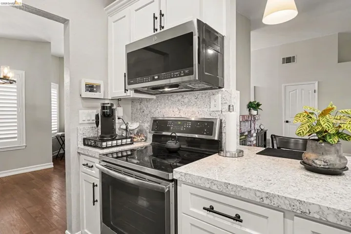 Contemporary kitchen featuring white cabinetry with matte black hardware, stainless steel appliances including a range and microwave, light-toned countertops, and a coordinating backsplash