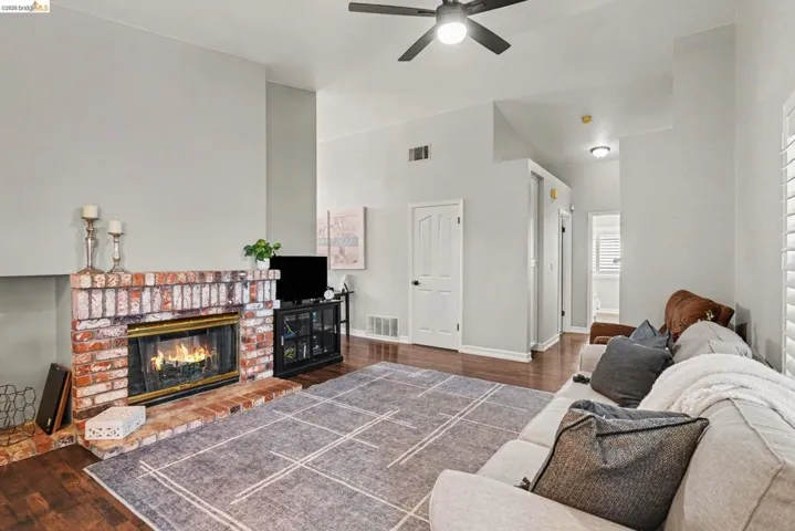 Living area featuring a brick fireplace, wood-finish flooring, vaulted ceilings, and a ceiling fan