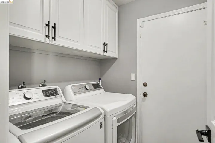 Dedicated laundry area featuring white shaker-style cabinetry with matte black hardware