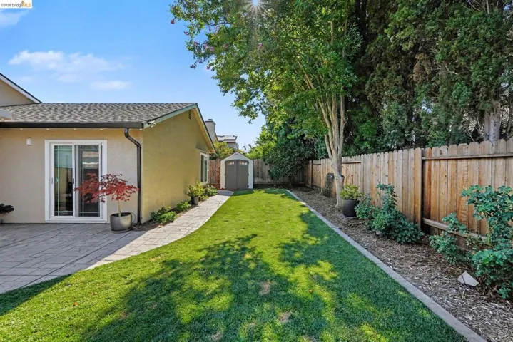 Spacious backyard featuring a manicured lawn, stamped concrete patio, sliding glass door access, a storage shed, and a privacy fence