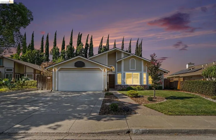 Two-story residence featuring a two-car garage, concrete driveway, and a manicured lawn with mature landscaping