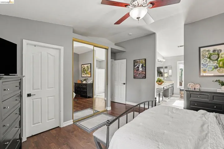Bedroom featuring wood-finish flooring, a ceiling fan with light fixture, and a mirrored closet with gold-tone framing