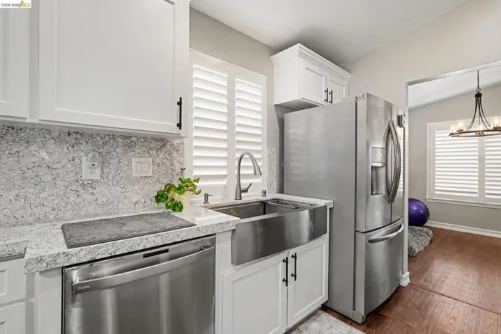 White shaker cabinetry paired with stainless steel appliances, a farmhouse sink, and a speckled countertop