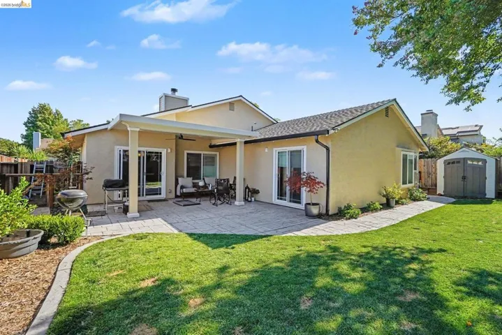 Expansive backyard featuring a manicured lawn, a paved patio, and a covered outdoor living area