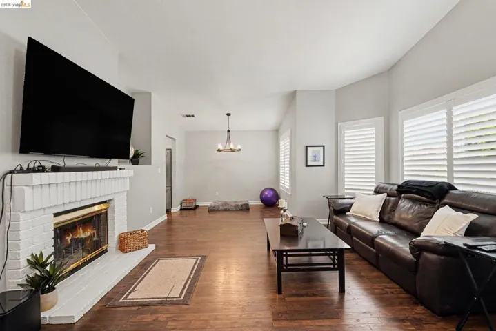 Spacious living area featuring rich wood-finish flooring and a white brick fireplace with a hearth